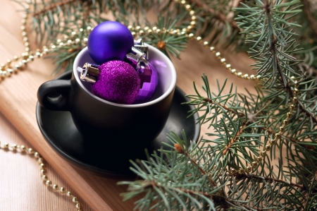 Festive Christmas still life made of a black tea cup filled with pink and violet decoration balls near a decorated fir tree branch against a wooden table. Copy spaceの写真素材