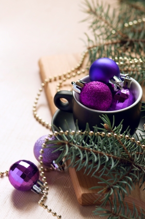Festive Christmas still life made of a black tea cup filled with pink and violet decoration balls near a decorated fir tree branch against a wooden table. Copy spaceの写真素材