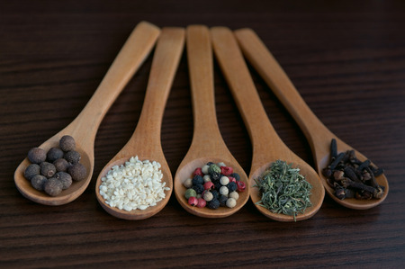 Wooden spoons on a table with a selection of different spices in them like allspices, sesame, red,...