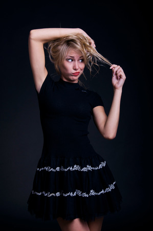 Blond woman model wearing black dress, holding her curly hair, looking at with surprise and disappointment. Over blackbackgroundの写真素材