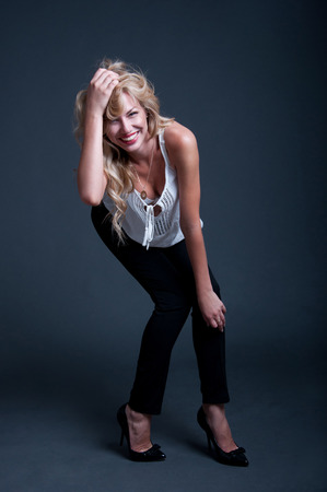 Pretty happy confident blond business woman wearing high heels, white top and black pants, red lipstick, hair made in locks, laughing, posing, looking at camera, smiling with toothy smile. Over gray backgroundの写真素材