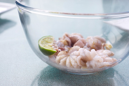 Fresh baby octopus being pickled with lime slice, garlic and olive oil in a glass bowl before...