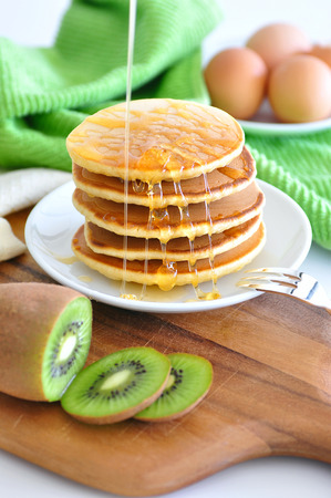 Delicious golden pancakes cooked on dry pan and served for breakfast with honey and kiwi fruit on a wooden board. Still life, copy spaceの写真素材