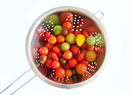 Colorful red yellow and green cherry tomatoes washed in a stainless colander, isolated on white...