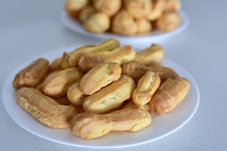 Home made freshly baked crispy oblong pastry eclairs on a round plate, main focus on an eclair in...