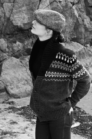 Black white profile portrait of beautiful brunette woman model in boyish clothes like turtleneck sweater, knitted jacket, jeans, cap, holding hands in pockets, looking up. Against rocks backgroundの写真素材