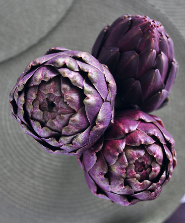 A bunch of beautiful fresh purple artichokes in a transparent jar on a table with round green table rugs, top viewの写真素材