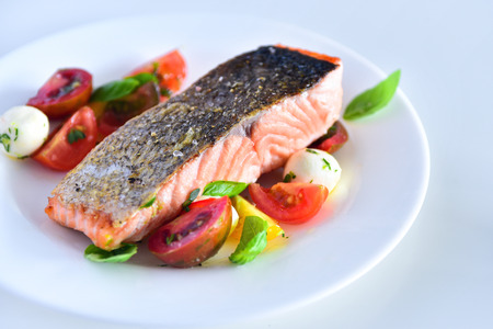 Delicious salmon steak with golden crispy skin served with basil leaves, fresh tomato and bocconcini cheese salad and herb infused oilの写真素材