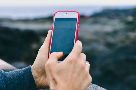 A man taking picture of rocks and landscape with his mobile phone with vertical orientation, main focus on hands and phone.の写真素材