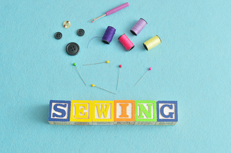 The word sewing spelled with colorful alphabet blocks displayed with spools of thread and various needlework accessories against a blue backgroundの写真素材