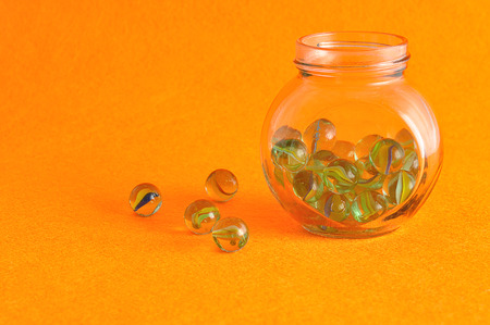 A collection of marbles in a glass jar displayed on an orange backgroundの写真素材