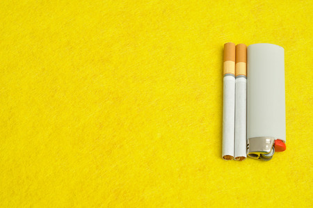 A white lighter with two cigarettes displayed on a yellow backgroundの写真素材
