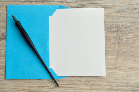 A blue envelope with a piece of paper sticking out to write a message displayed with a fountain pen on a wooden tableの写真素材
