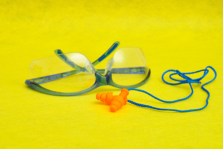 Safety goggles and ear plugs isolated on a yellow background
