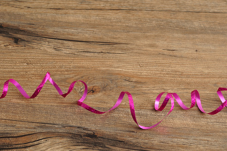 A pink ribbon coiled up on a wooden backgroundの写真素材