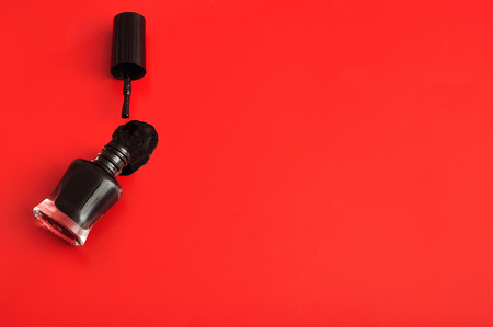 An open bottle of black nail polish displayed with its brush on a red backgroundの写真素材