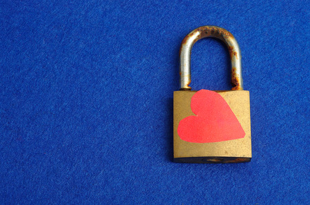 A rusty old pad lock decorated with a red heart displayed on a blue backgroundの写真素材