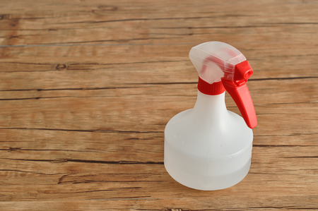 A white spray bottle with a red trigger isolated against a wooden background