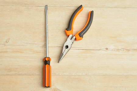A long nose pliers and a screw driver on a wooden backgroundの写真素材