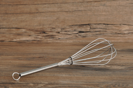 Egg beater, whisk, isolated on a wooden background