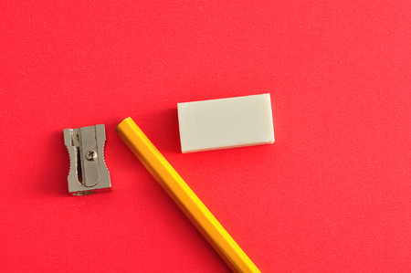 A sharpener, eraser and yellow pencil isolated on a red background
