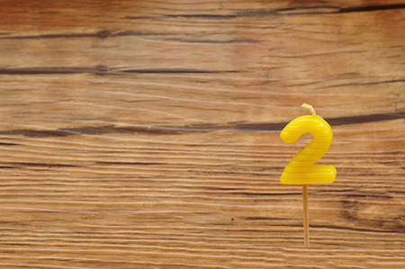 A birth day candle isolated on a wooden background. Yellow number two