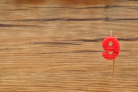 A birth day candle isolated on a wooden background. Red number nine