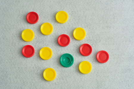 A variety of yellow and red plastic discs with only one green on a white background