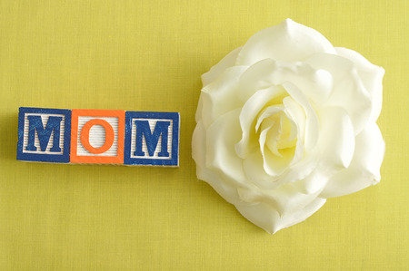 Mom spelled with alphabet blocks and a white artificial rose on a yellow backgroundの写真素材