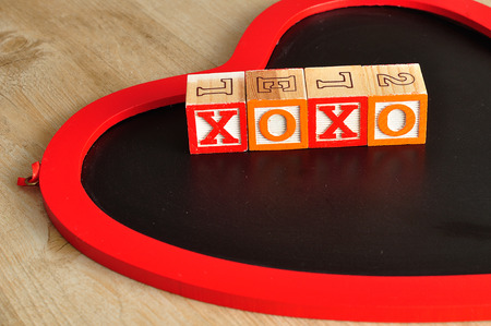 Valentine's Day. XOXO Spelled with colorful alphabet blocks and a chalk board in the shape of a red heartの写真素材