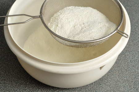 Sifting flour into a white plastic bowl