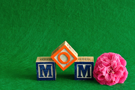The word mom spelled with alphabet blocks against a green background with a pink flowerの写真素材