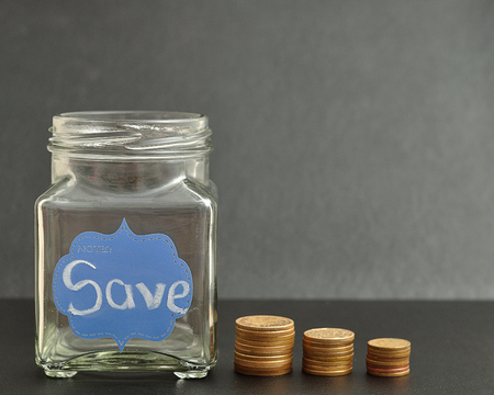 An empty jar with the word save on it and coins stack next to it