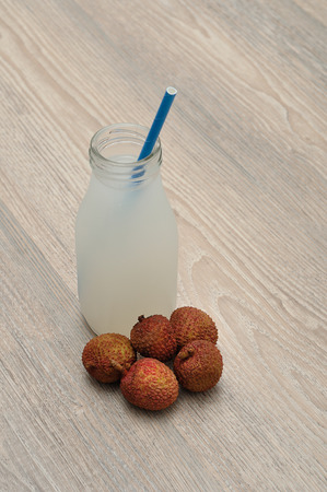 Litchi juice in a glass bottle with a blue straw and fresh litchis . の写真素材