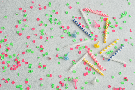 Birthday candles displayed on a white background littered with green and pink confettiの写真素材