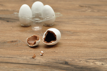 A white chocolate coated easter egg broken into pieces with a container with three whole ones in the...