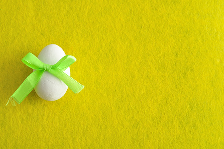 A white easter egg with a green bow isolated on a yellow backgroundの写真素材