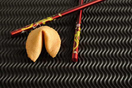 A fortune cookie and a pair of red chopsticks isolated on a black backgroundの写真素材