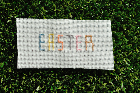 Easter cross stitched on textile isolated on artificial grassの写真素材