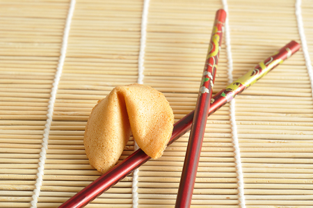 A fortune cookie with red chopsticks isolated on a bamboo backgroundの写真素材