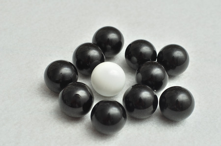 One white and a lot of black balls displayed on a white backgroundの写真素材
