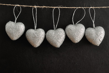 Valentines day. A row of silver hearts hanging on a rope isolated against a black background