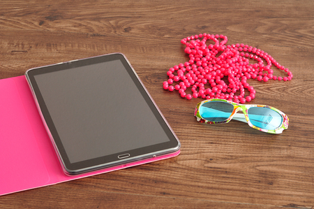 A tablet in a pink holder displayed with pink beads and sunglassesの写真素材