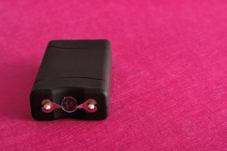 A black taser isolated against a pink background