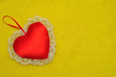 A red satin heart with white lace displayed on a yellow backgroundの写真素材
