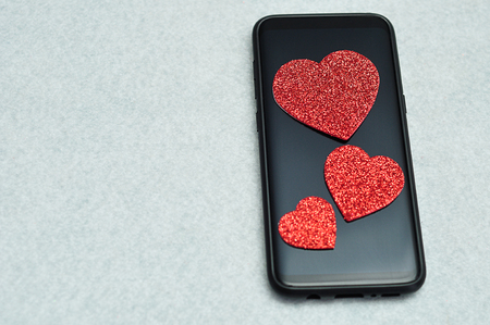 A smart phone displayed with three red glitter heartsの写真素材