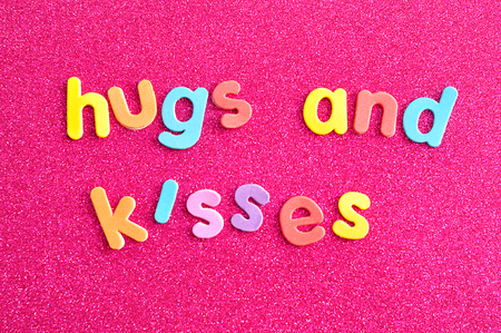 The words hugs and kisses on colorful letters on a pink backgroundの写真素材