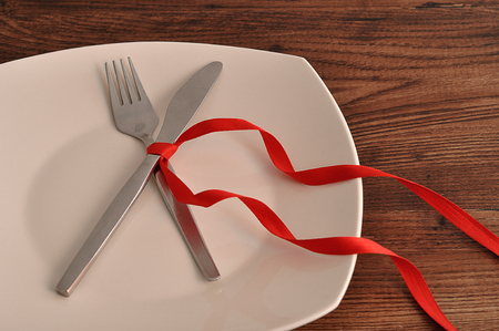 A fork an knife tied together with a red ribbon displayed on a white plateの写真素材