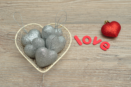 A wire basket filled with silver heart shape baubles and the word love and a red baubleの写真素材