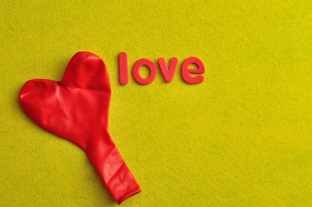 A red heart shape balloon and the word love on a yellow backgroundの写真素材